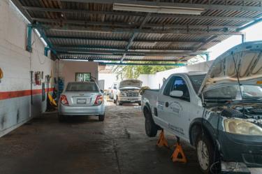 Dos automóviles siendo arreglados al interior de un taller mecánico.
